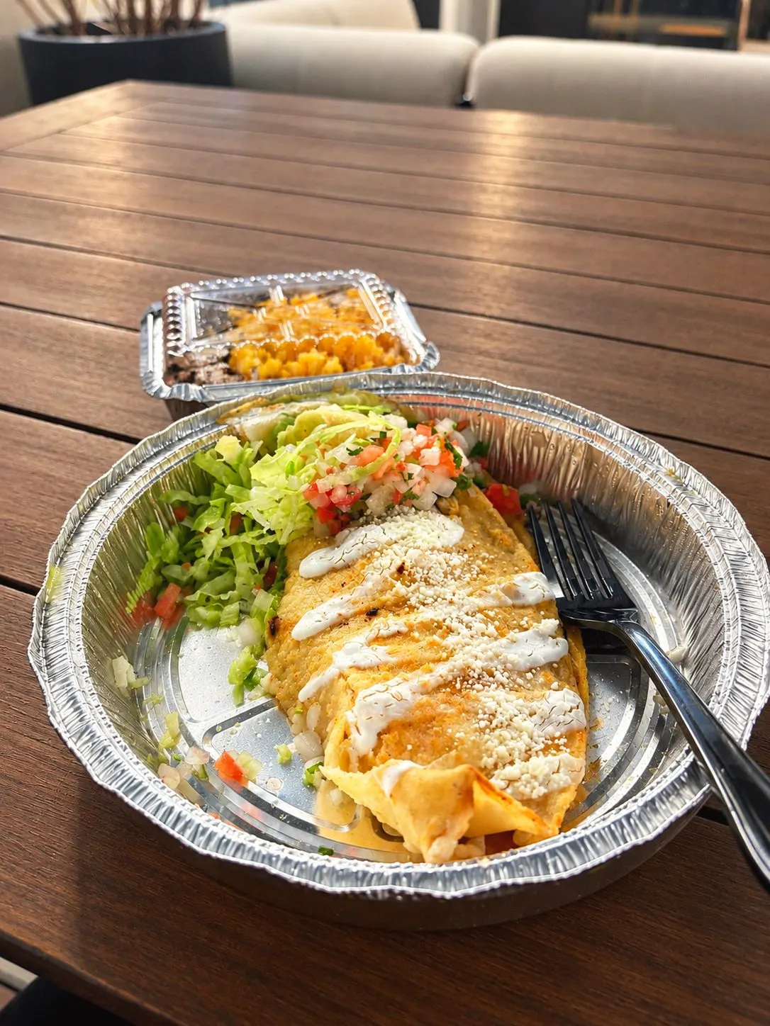 Veggie quesadilla with crema, cotija, lettuce and pico de gallo in a takeout tray, with rice and beans behind